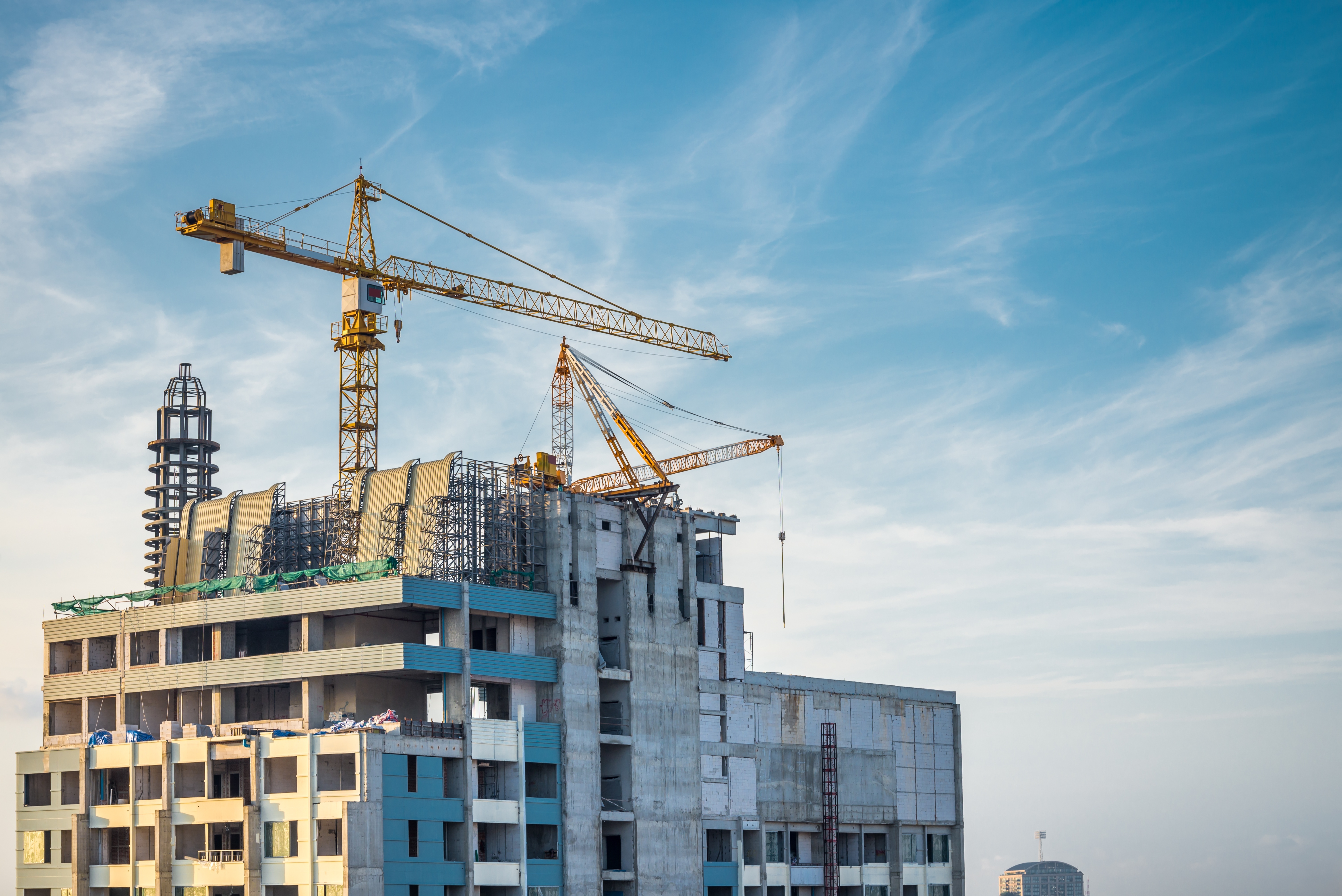 Construction site with multi-story residential buildings under development, featuring yellow tower cranes against a blue sky.