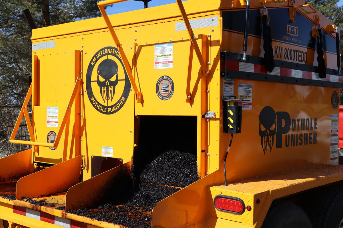 Yellow and orange pothole repair machine with skull logo and 'Pothole Punisher' branding