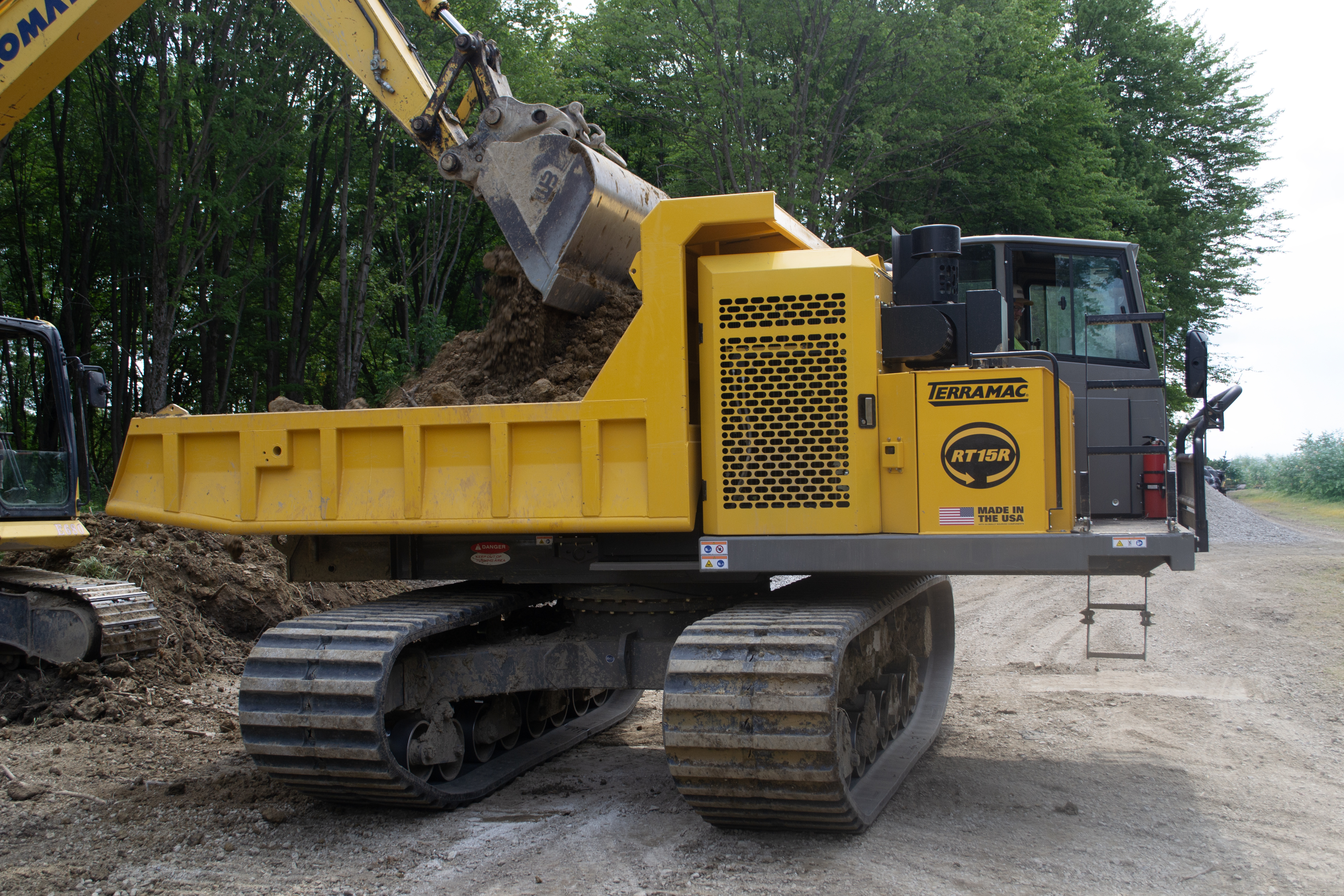 Yellow Terramac tracked dump truck with excavator bucket loading soil at construction site