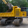 Yellow Terramac tracked dump truck with excavator bucket loading soil at construction site