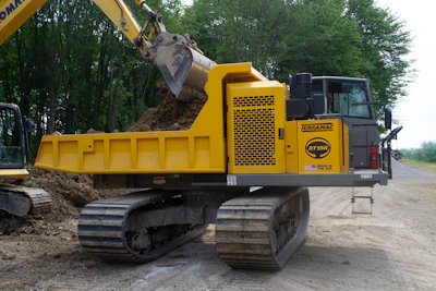 Yellow Terramac tracked dump truck with excavator bucket loading soil at construction site