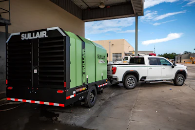 Sullair electric air compressor trailer with green and black exterior parked beside white pickup truck at industrial facility