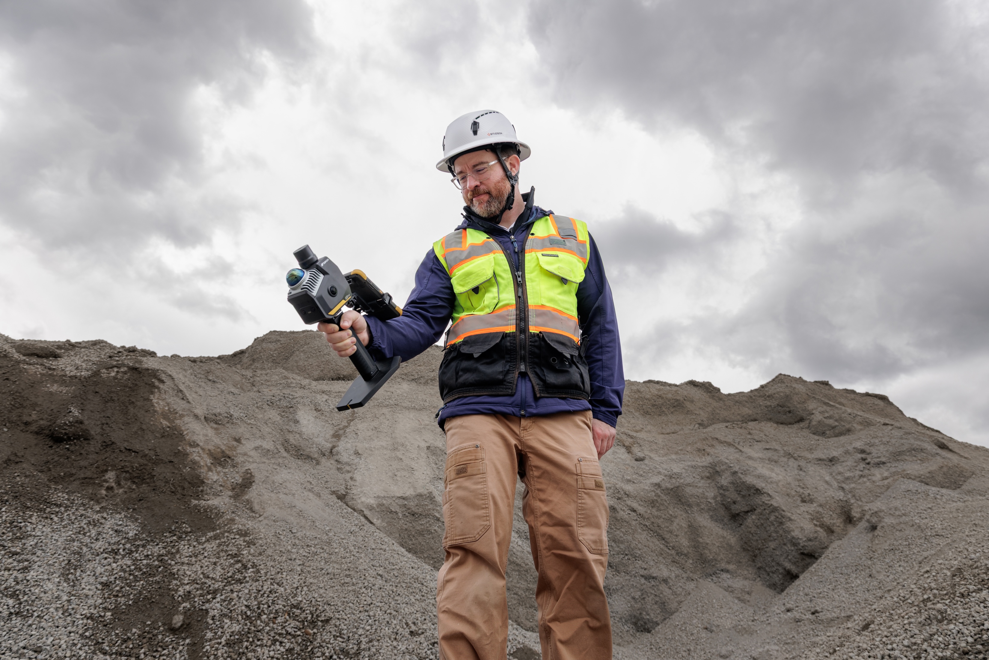 Construction worker in safety gear holding thermal imaging camera on gravel site
