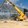 Yellow Liebherr telehandler lifting materials at construction site with metal framework building