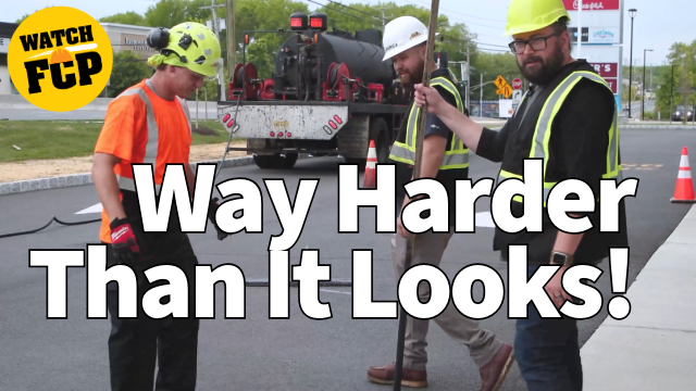 Construction workers in safety gear discussing road work project with equipment truck in background