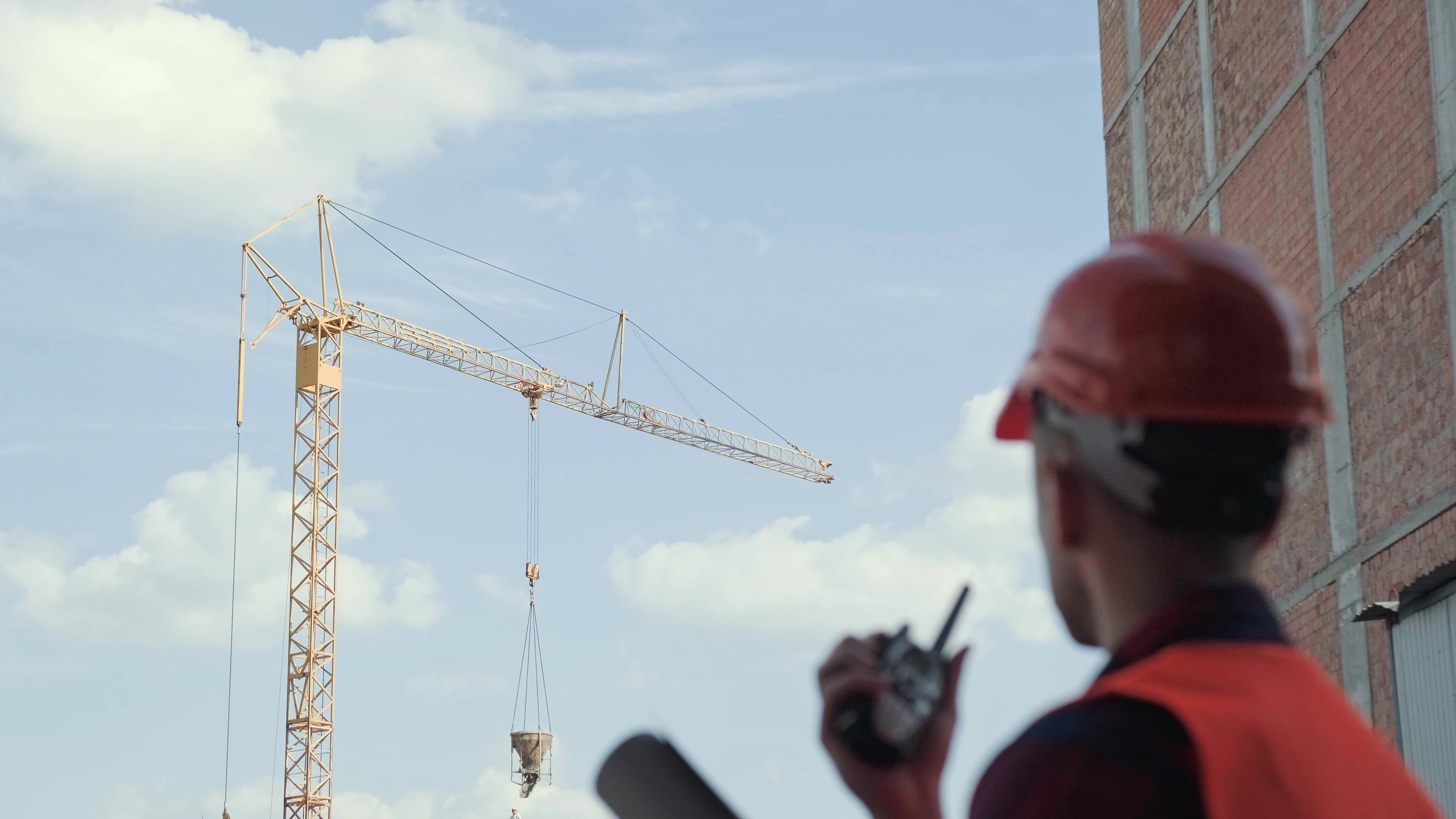 Construction worker in red safety gear operating tower crane at building site