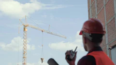 Construction worker in red safety gear operating tower crane at building site