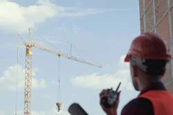 Construction worker in red safety gear operating tower crane at building site