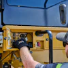 Technician in safety gear inspecting yellow heavy equipment control panel with blue cab visible above