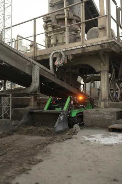Green heavy machinery loader operating at industrial construction site beneath concrete infrastructure