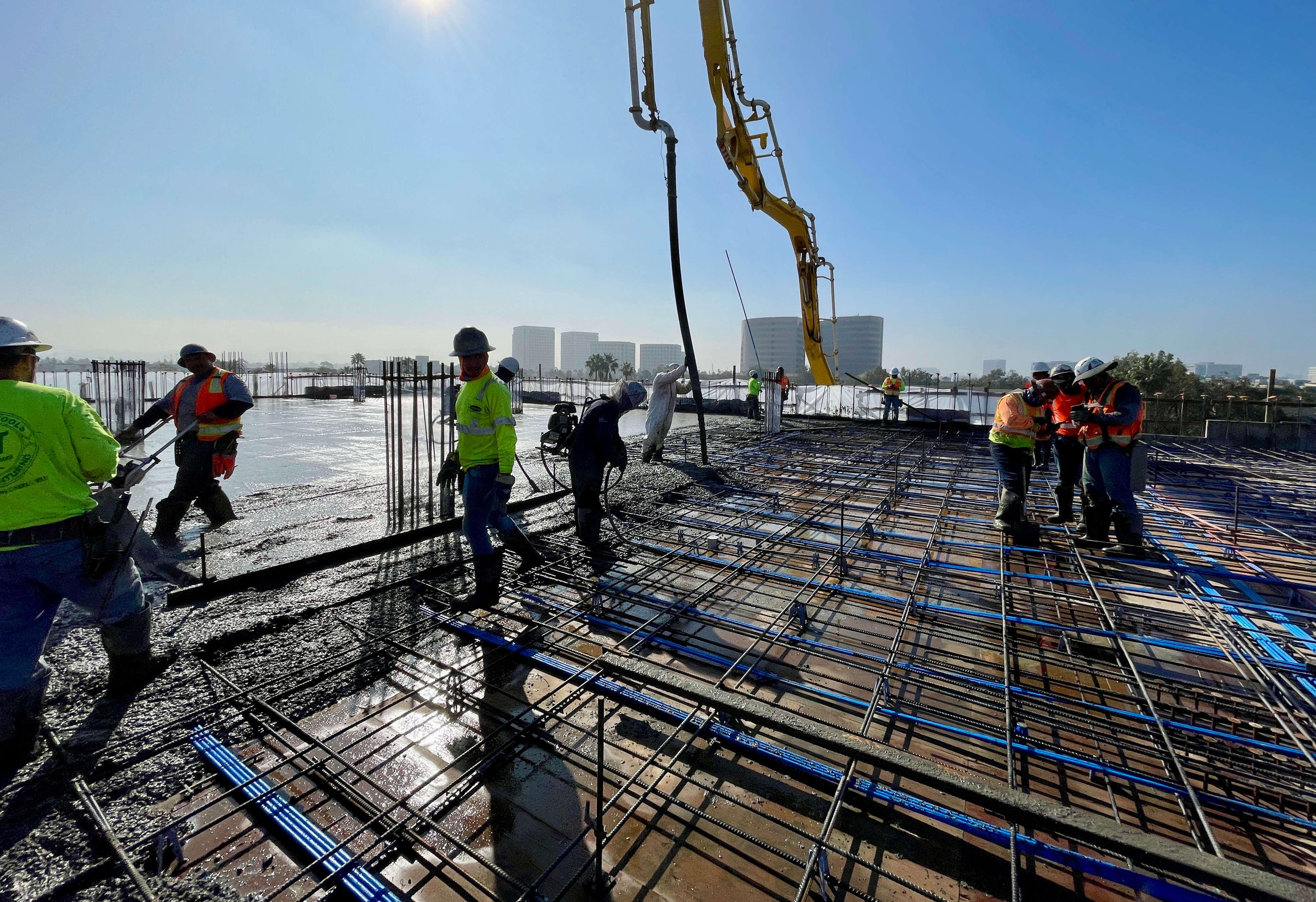 Construction workers pouring concrete on rooftop with city skyline and crane in background