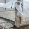 Greenhouse structure with white mesh netting and concrete foundation under construction