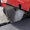 Red asphalt cutting machine with circular saw blade cutting through road pavement