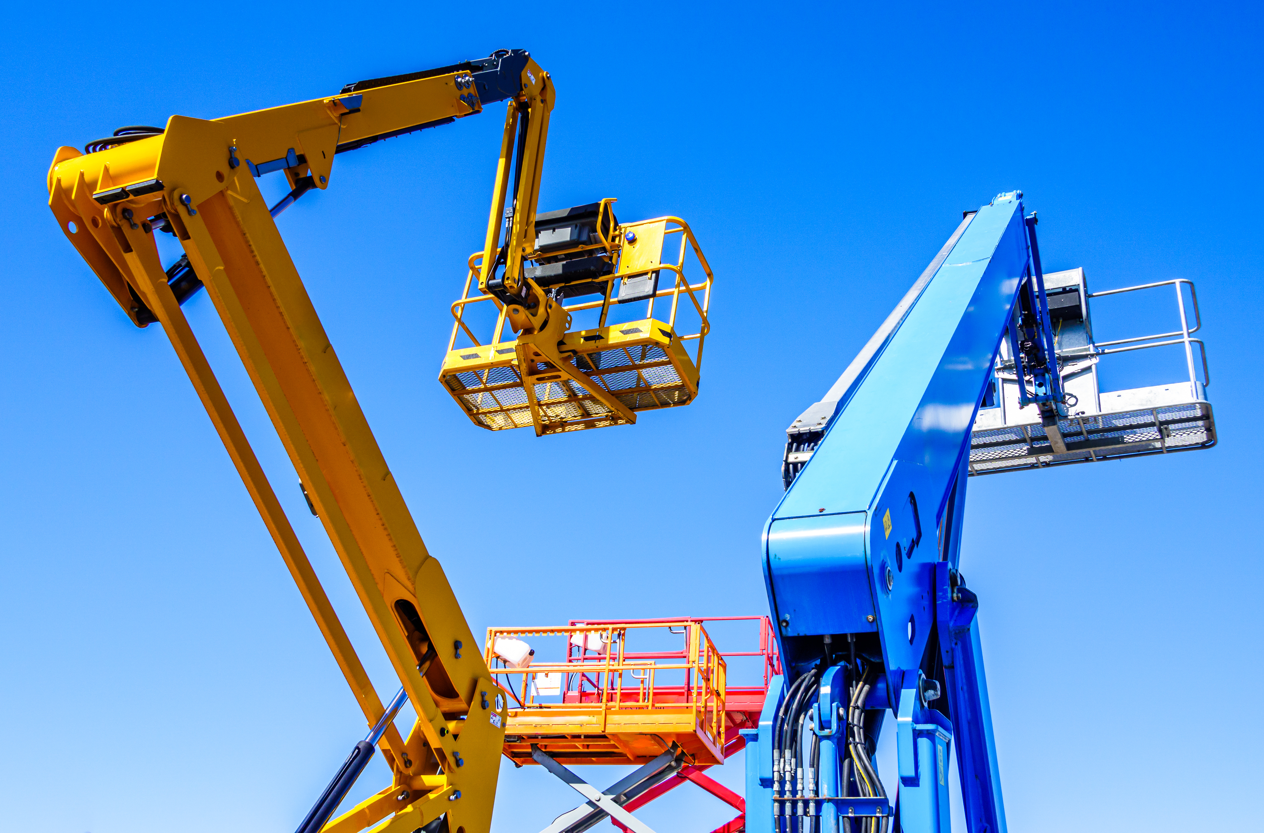 Yellow and blue aerial work platforms with extended booms and safety baskets against clear blue sky