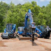 Blue construction equipment including excavator and skid steer loaders positioned at a dirt job site with trees in background
