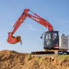 Red Link-Belt excavator with extended boom and bucket digging into dirt pile under blue sky