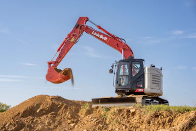 Red Link-Belt excavator with extended boom and bucket digging into dirt pile under blue sky