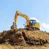 Yellow Komatsu excavator digging earth on construction site under blue sky with white clouds