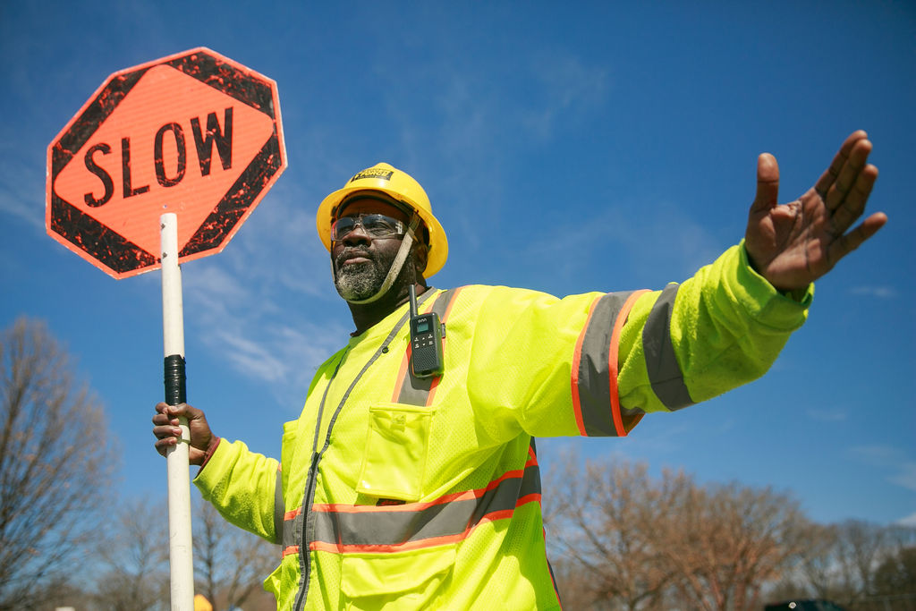 Construction worker in safety gear holding an orange SLOW traffic sign against blue sky