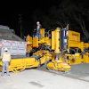 Gomaco concrete paving machine operating at night with workers and dump truck during road construction.