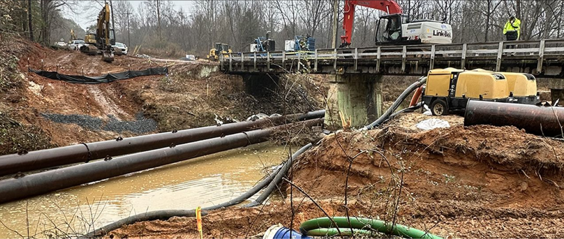 Construction site with large pipes, excavator, and bridge during water infrastructure installation project