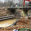 Construction site with large pipes, excavator, and bridge during water infrastructure installation project