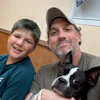 Man and boy smiling with black and white dog indoors