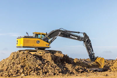 Yellow John Deere excavator on a dirt pile against a clear blue sky