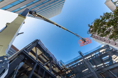 Construction crane lifting red safety basket above steel framework and solar panels on clear day