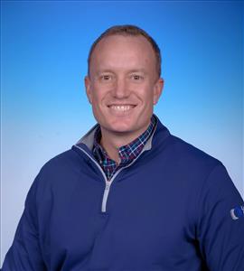 Professional headshot of a smiling man in navy quarter-zip pullover against blue gradient background Headshot