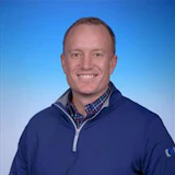 Professional headshot of a smiling man in navy quarter-zip pullover against blue gradient background