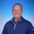 Professional headshot of a smiling man in navy quarter-zip pullover against blue gradient background Headshot