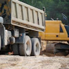 Construction site with white dump truck and yellow excavator on dirt ground