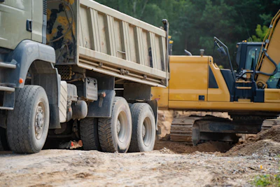 Construction site with white dump truck and yellow excavator on dirt ground