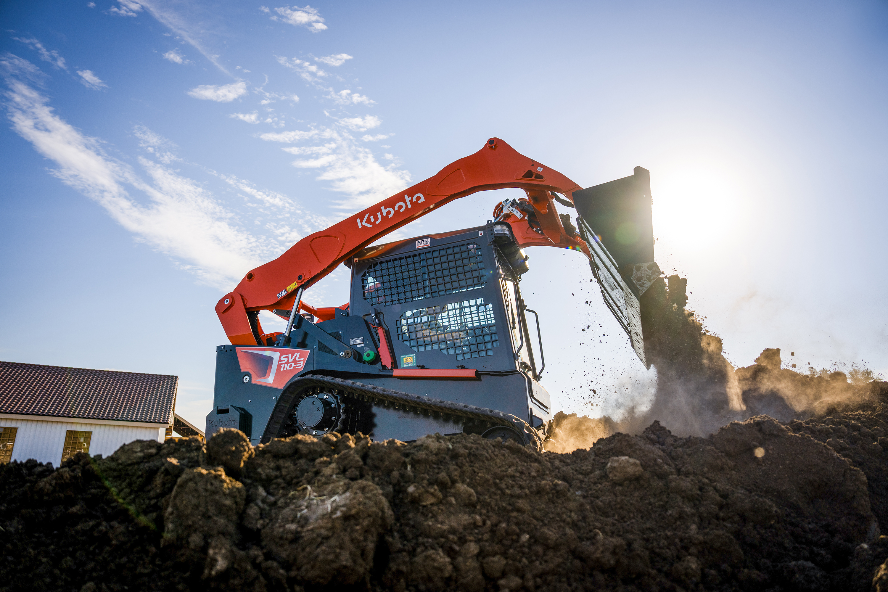 Kubota red and blue skid steer loader moving soil and debris on a construction site under clear sky