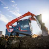Kubota red and blue skid steer loader moving soil and debris on a construction site under clear sky