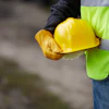 Construction worker holding yellow hard hat wearing neon safety vest and brown gloves