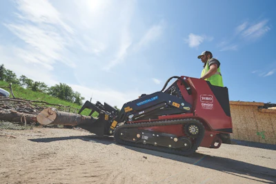 Worker operating a Toro wood chipper on a construction site with logs and materials nearby
