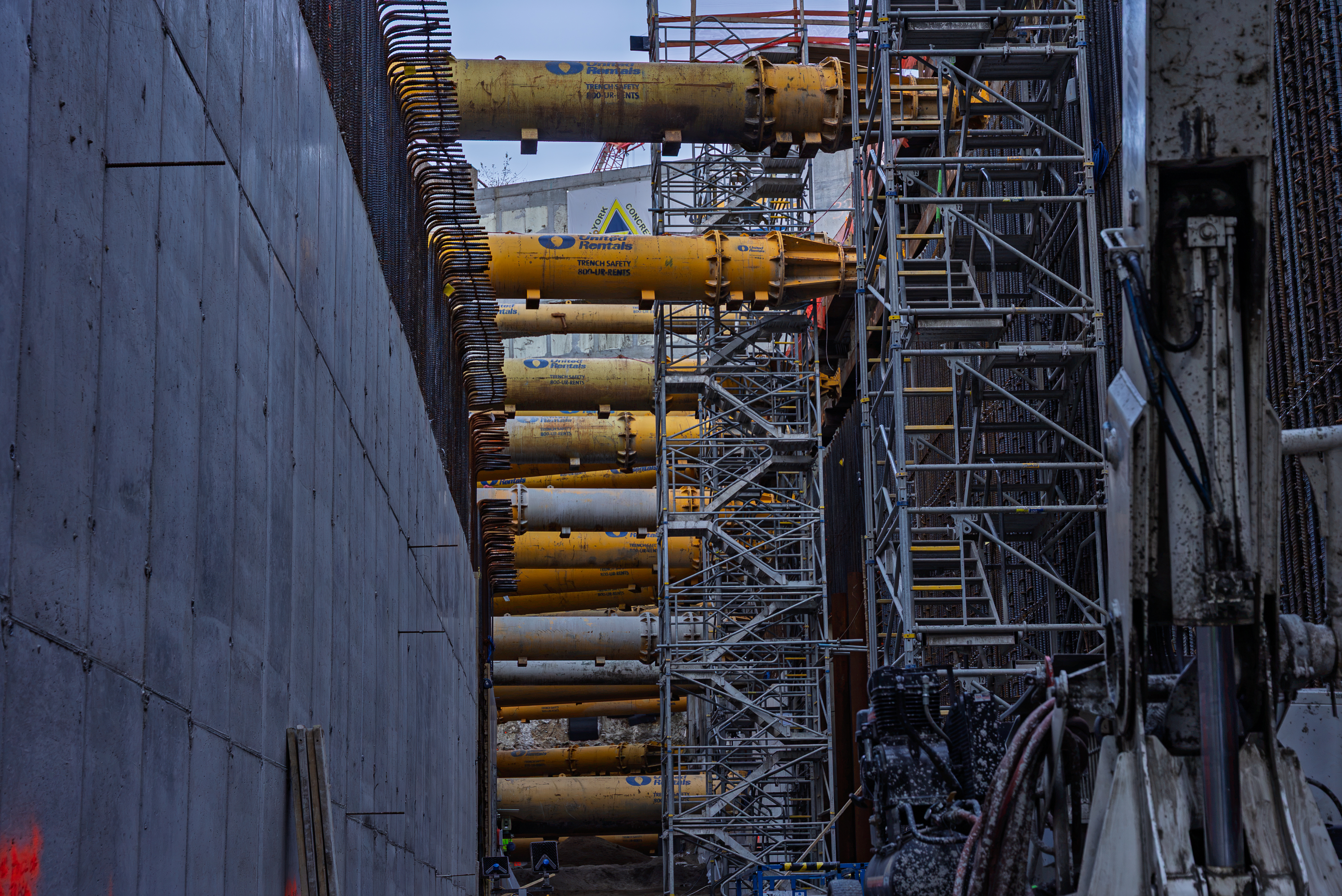 Industrial construction site with yellow hydraulic cylinders mounted on steel scaffolding and concrete walls