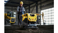 Construction worker operating yellow Wacker Neuson compactor in industrial warehouse setting