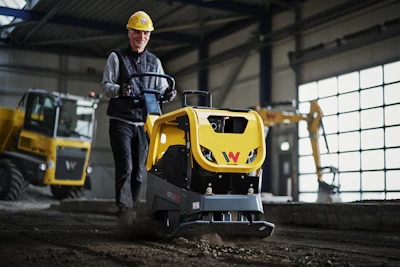 Construction worker operating yellow Wacker Neuson compactor in industrial warehouse setting