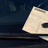 Parking violation ticket placed under windshield wiper blade on dark vehicle
