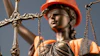 Lady Justice statue wearing orange hard hat and safety vest, holding brass scales against blue sky