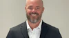 Professional headshot of a smiling man in dark blazer and white shirt against neutral background