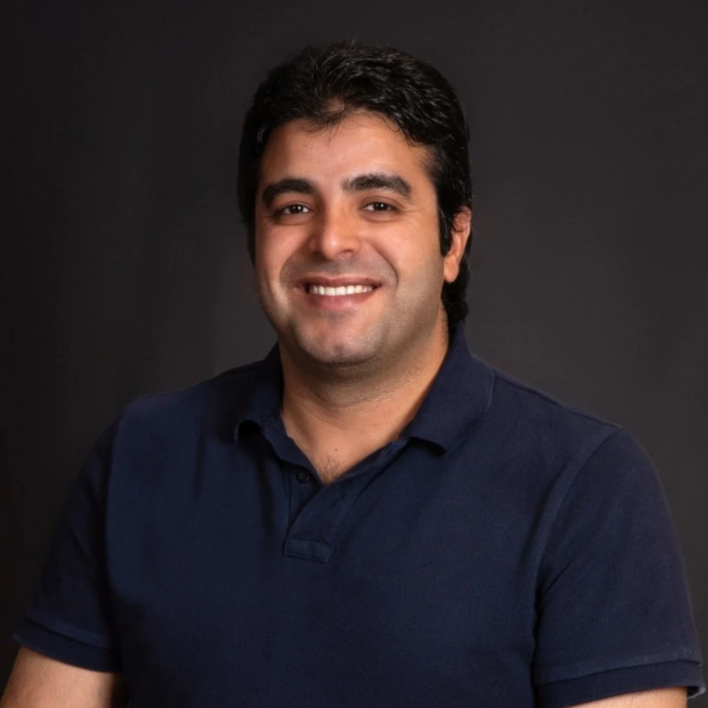 Professional headshot of a man in navy polo shirt smiling against dark background