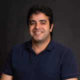 Professional headshot of a man in navy polo shirt smiling against dark background